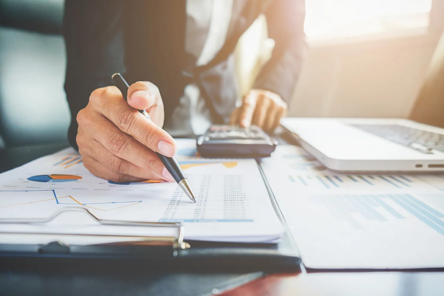 Financial advisor pointing a pen at charts and reports on a clipboard while using a calculator